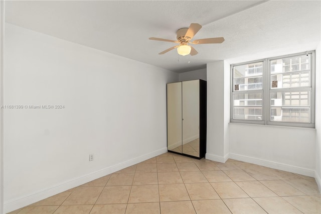 unfurnished bedroom with a textured ceiling, baseboards, ceiling fan, and light tile patterned floors