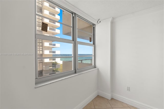 empty room with ornamental molding, light tile patterned flooring, baseboards, a textured ceiling, and a water view