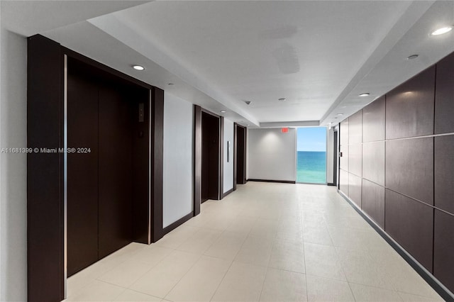corridor with baseboards, elevator, a water view, a tray ceiling, and recessed lighting
