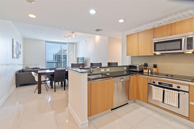 kitchen featuring decorative backsplash, kitchen peninsula, stainless steel appliances, sink, and light tile patterned floors