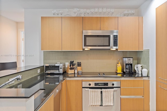 kitchen featuring light brown cabinetry, appliances with stainless steel finishes, backsplash, and dark stone countertops