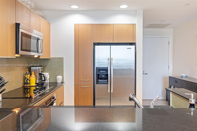 kitchen featuring dark stone countertops, appliances with stainless steel finishes, kitchen peninsula, and decorative backsplash