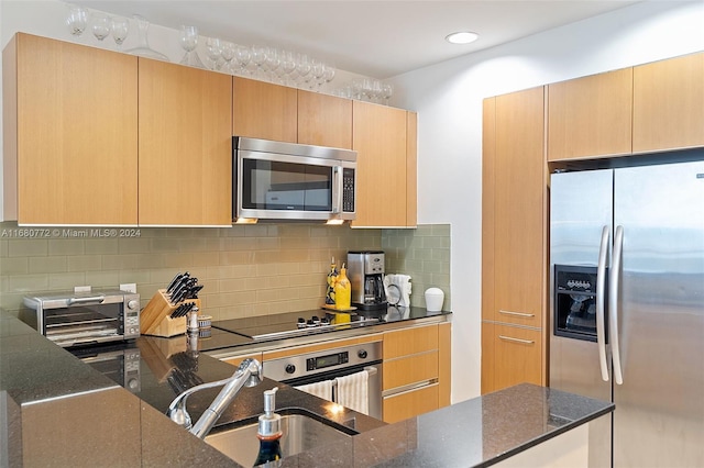 kitchen featuring appliances with stainless steel finishes, light brown cabinets, decorative backsplash, and dark stone countertops