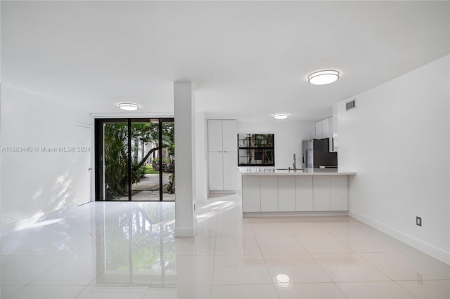 kitchen featuring white cabinetry, sink, light tile patterned floors, and stainless steel refrigerator