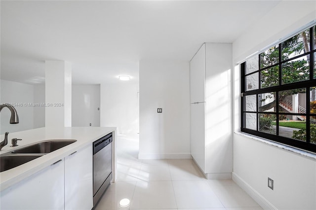 kitchen with white cabinetry, stainless steel dishwasher, sink, and light tile patterned floors