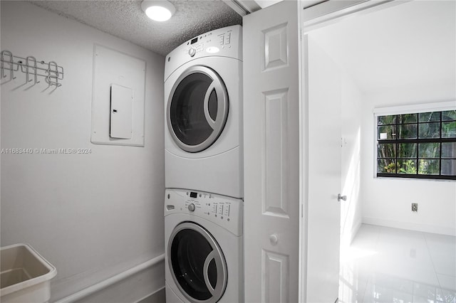 clothes washing area with tile patterned flooring, a textured ceiling, and stacked washer and clothes dryer