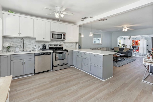 kitchen with hanging light fixtures, kitchen peninsula, sink, white cabinets, and appliances with stainless steel finishes