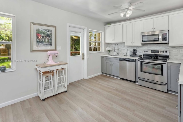 kitchen with appliances with stainless steel finishes, a wealth of natural light, gray cabinets, and white cabinets