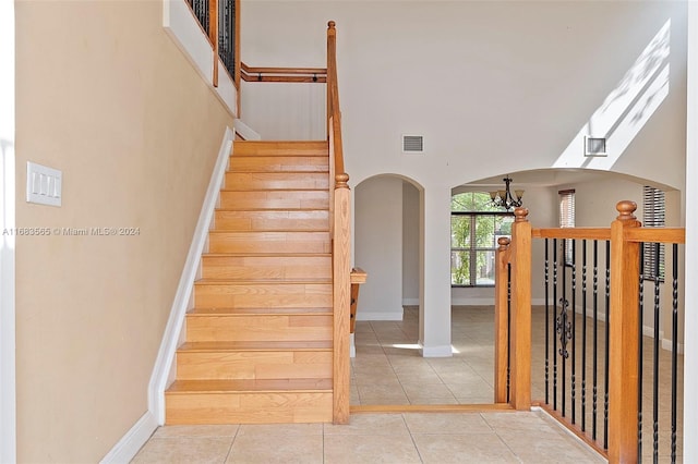 stairway with a chandelier, tile patterned floors, and a high ceiling