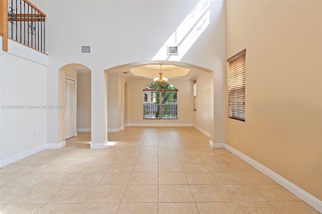 empty room featuring light tile patterned flooring, a high ceiling, and a chandelier