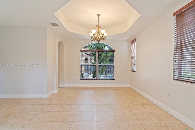 unfurnished room featuring a notable chandelier, a raised ceiling, and light tile patterned floors