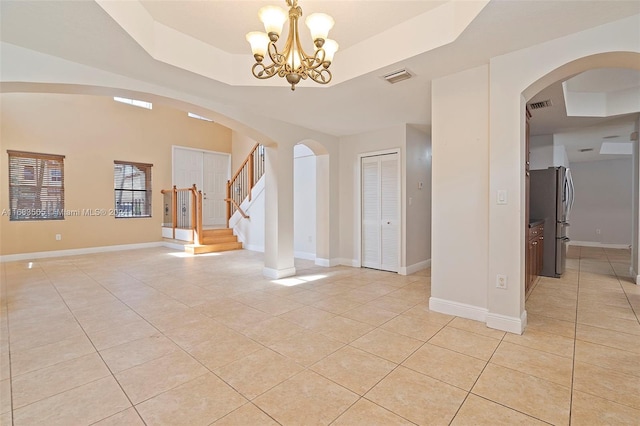 empty room with an inviting chandelier, light tile patterned flooring, and a raised ceiling