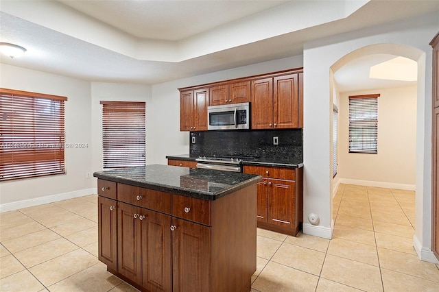 kitchen featuring tasteful backsplash, appliances with stainless steel finishes, a kitchen island, dark stone countertops, and light tile patterned floors