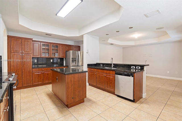 kitchen with a kitchen island, a tray ceiling, stainless steel appliances, dark stone counters, and sink