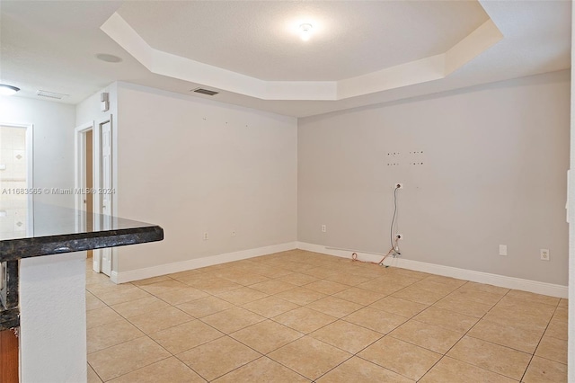 unfurnished room with a raised ceiling and light tile patterned floors