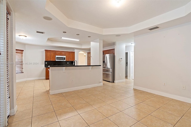 kitchen with a kitchen breakfast bar, stainless steel appliances, light tile patterned floors, a raised ceiling, and a textured ceiling