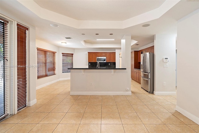 kitchen with a breakfast bar, light tile patterned floors, stainless steel appliances, and a tray ceiling