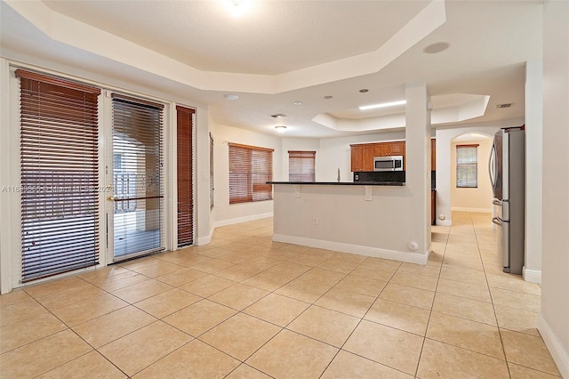 kitchen featuring appliances with stainless steel finishes, a raised ceiling, kitchen peninsula, a kitchen breakfast bar, and light tile patterned floors