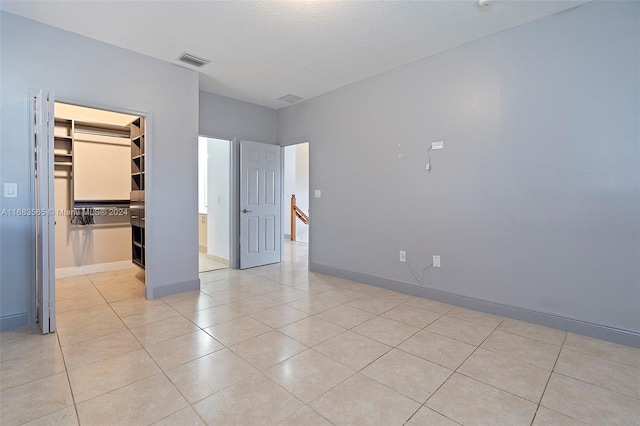 unfurnished bedroom featuring a closet, a textured ceiling, light tile patterned floors, and a walk in closet