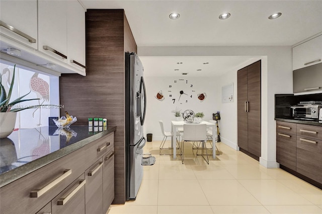 kitchen with light tile patterned floors, stainless steel refrigerator, and dark stone counters