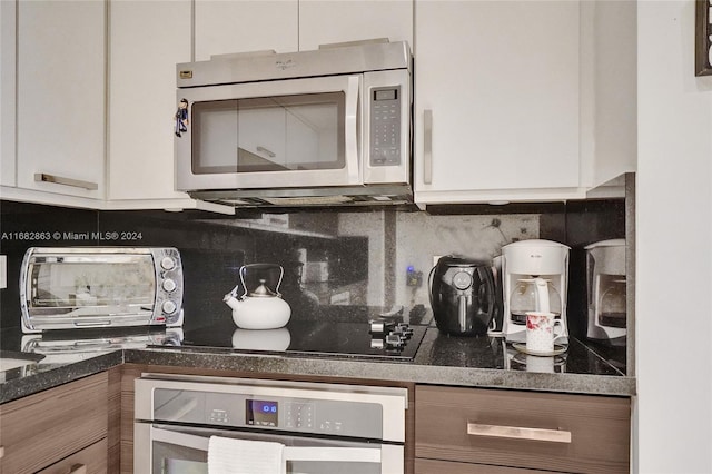 kitchen featuring stainless steel appliances, decorative backsplash, dark stone counters, and white cabinets