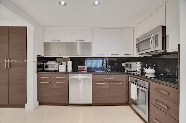 kitchen featuring stainless steel appliances, dark stone counters, white cabinets, decorative backsplash, and light tile patterned floors