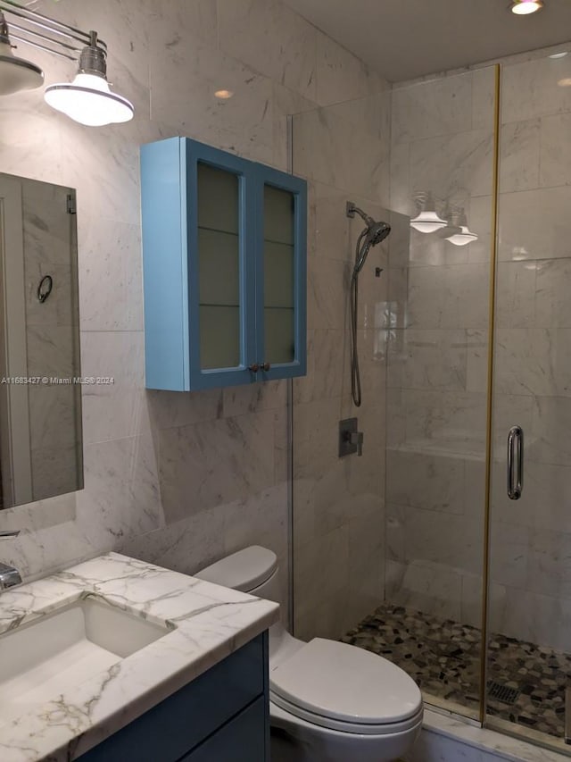 bathroom with a shower with door, toilet, tile walls, vanity, and tasteful backsplash