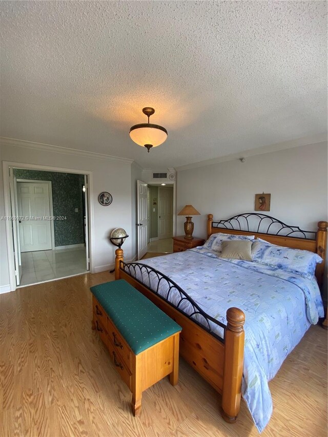 bedroom featuring crown molding, a textured ceiling, and light wood-type flooring