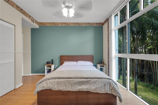 bedroom featuring light hardwood / wood-style flooring, ceiling fan, a closet, and multiple windows