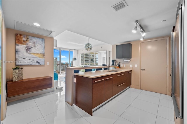 kitchen with kitchen peninsula, hanging light fixtures, light tile patterned floors, an inviting chandelier, and sink