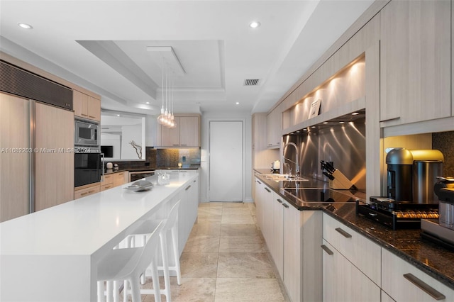 kitchen featuring light brown cabinets, tasteful backsplash, a raised ceiling, built in appliances, and pendant lighting