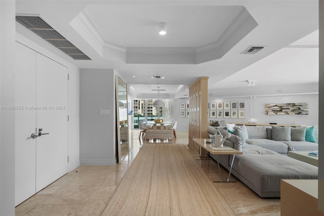 hall with light tile patterned floors, ornamental molding, and a tray ceiling