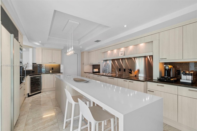 kitchen featuring a kitchen island, backsplash, beverage cooler, pendant lighting, and a raised ceiling