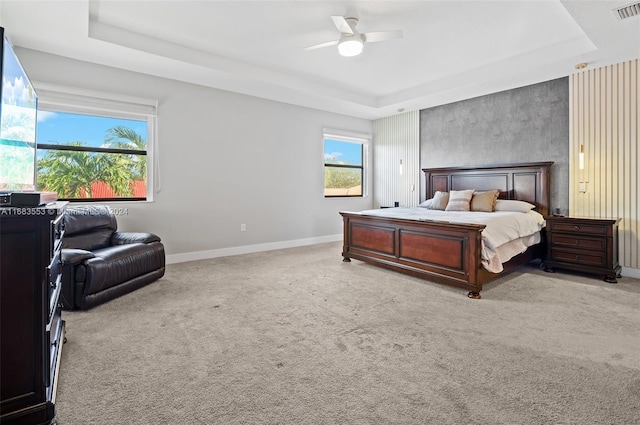 bedroom with ceiling fan, light carpet, and a tray ceiling