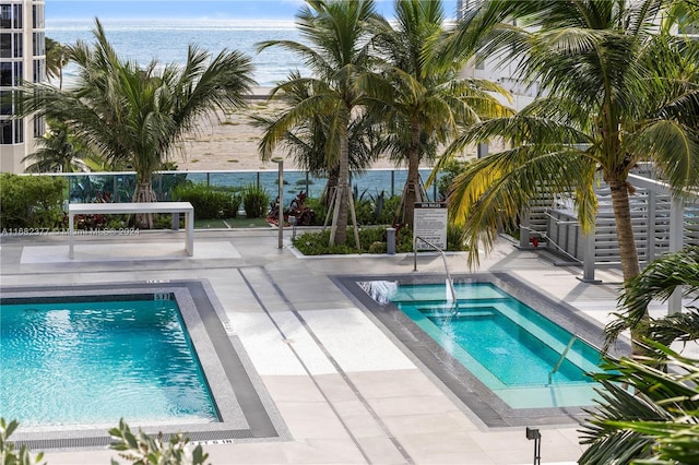 view of swimming pool with a patio, an in ground hot tub, and a water view