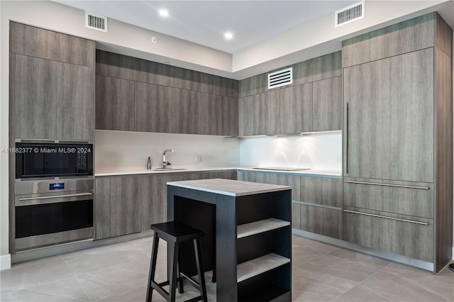 kitchen featuring a kitchen island, oven, sink, a breakfast bar, and light tile patterned floors