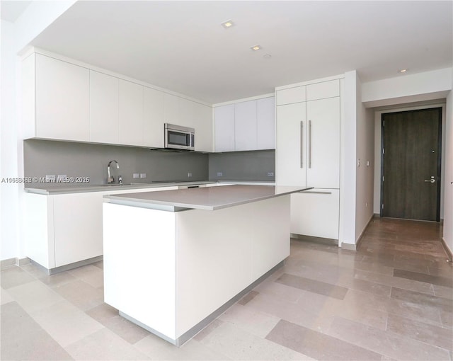 kitchen with light countertops, white cabinetry, stainless steel microwave, modern cabinets, and a center island