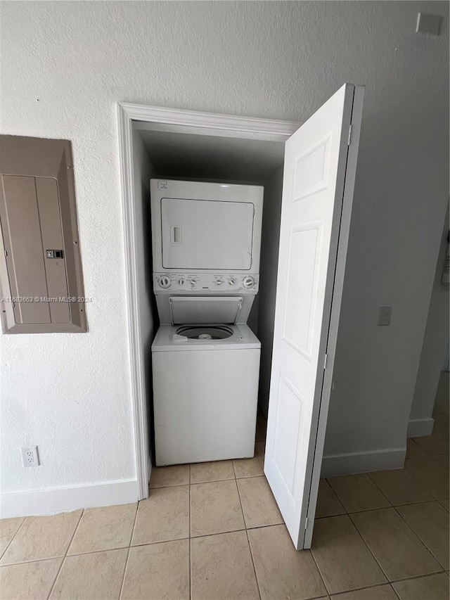 laundry area with stacked washer / drying machine, electric panel, and light tile patterned floors