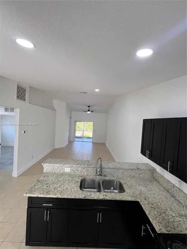 kitchen featuring lofted ceiling, light stone counters, ceiling fan, a textured ceiling, and sink