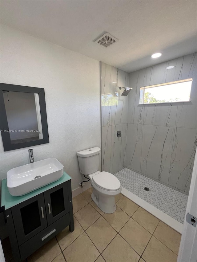 bathroom with vanity, a tile shower, toilet, and tile patterned floors