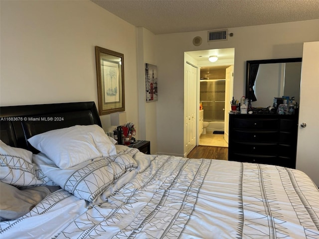 bedroom with ensuite bath, a textured ceiling, and hardwood / wood-style floors