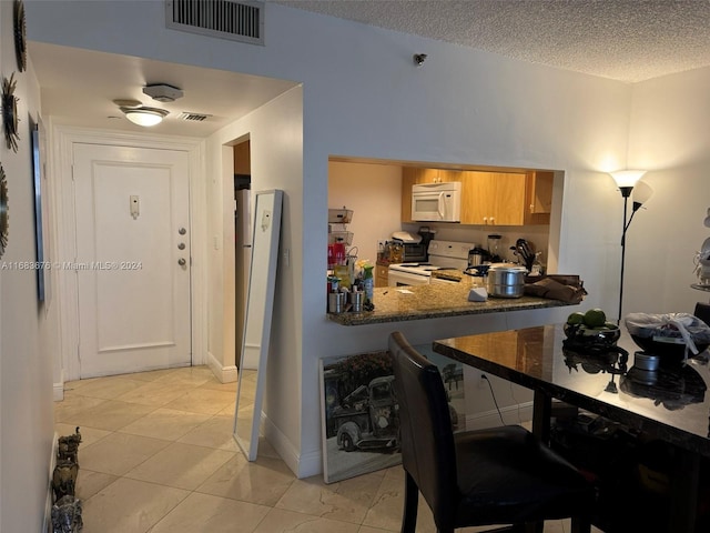 kitchen with a textured ceiling, white appliances, and light tile patterned floors