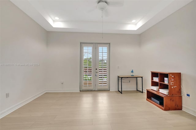 spare room featuring french doors, light hardwood / wood-style flooring, ceiling fan, and a raised ceiling