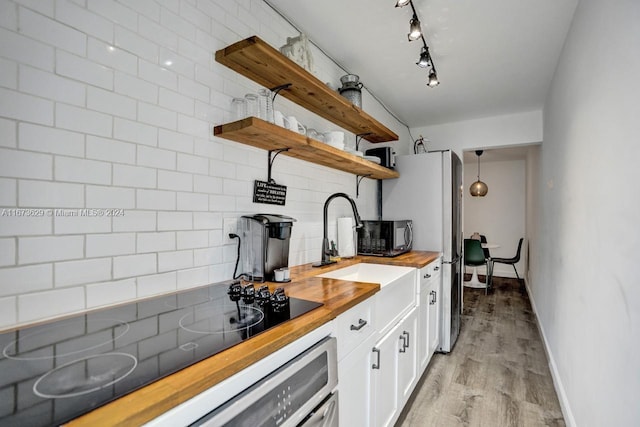 kitchen with decorative backsplash, white cabinets, pendant lighting, light wood-type flooring, and butcher block countertops