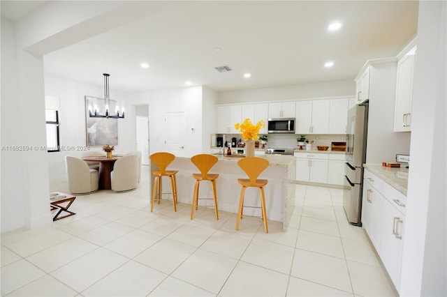 kitchen featuring a kitchen breakfast bar, stainless steel appliances, white cabinets, a notable chandelier, and a center island with sink