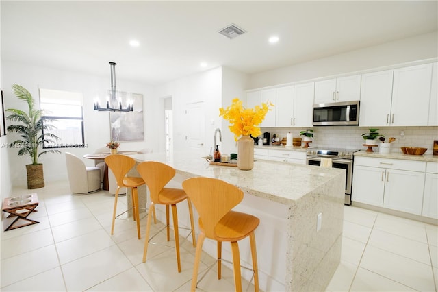 kitchen with an island with sink, hanging light fixtures, stainless steel appliances, white cabinets, and a breakfast bar area