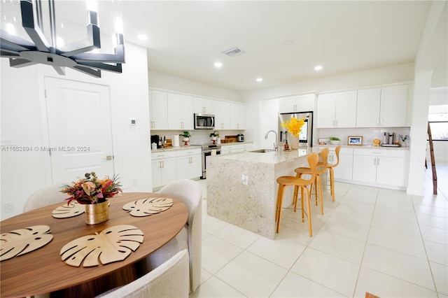 kitchen featuring white cabinets, stainless steel appliances, tasteful backsplash, and an island with sink