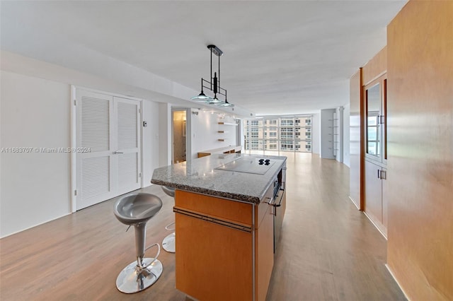 kitchen featuring a kitchen island, black electric stovetop, dark stone counters, pendant lighting, and light wood-type flooring