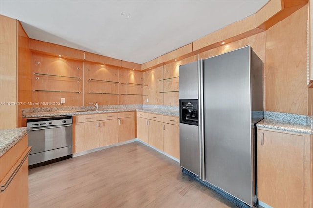 kitchen with light brown cabinets, sink, light stone countertops, appliances with stainless steel finishes, and light hardwood / wood-style floors