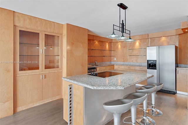 kitchen with hardwood / wood-style floors, stainless steel fridge with ice dispenser, a kitchen breakfast bar, light stone countertops, and pendant lighting